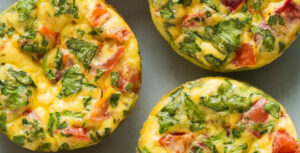 Overhead image of baked egg frittatas with small pieces of spinach and tomato throughout.
